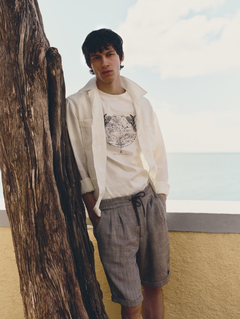 Kaplan wears a Brunello Cucinelli white linen Guayabera overshirt over a graphic tee with herringbone drawstring shorts by the coast