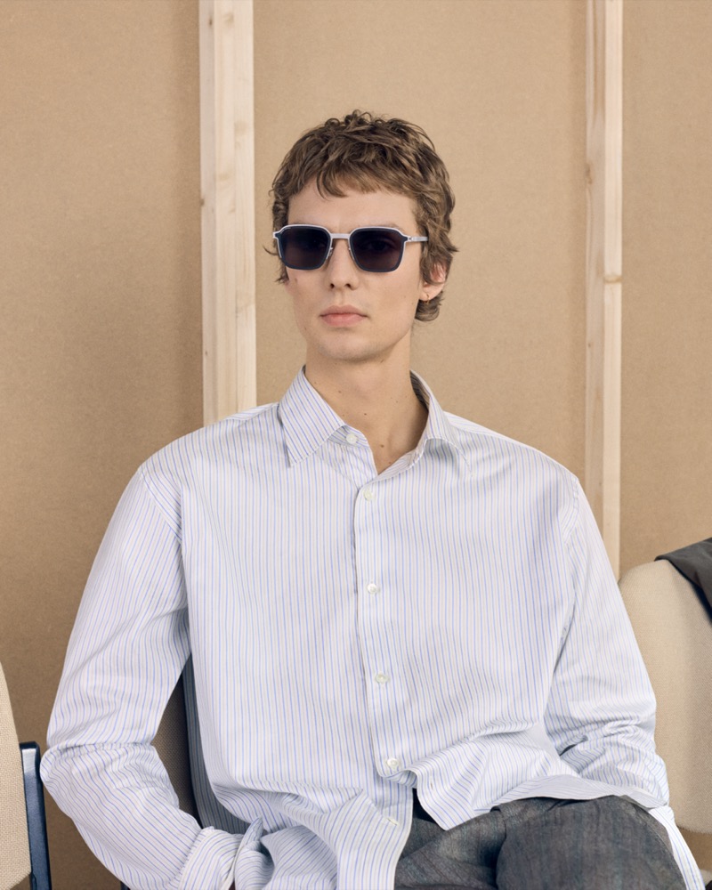 Leon Dame sits in a striped button-up shirt wearing MYKITA x RIMOWA sunglasses