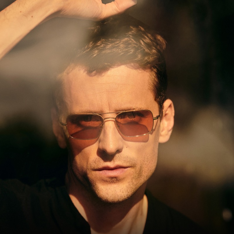 George wears Oliver Peoples Victory II gold double-bar navigator sunglasses with cognac lenses in direct sunlight