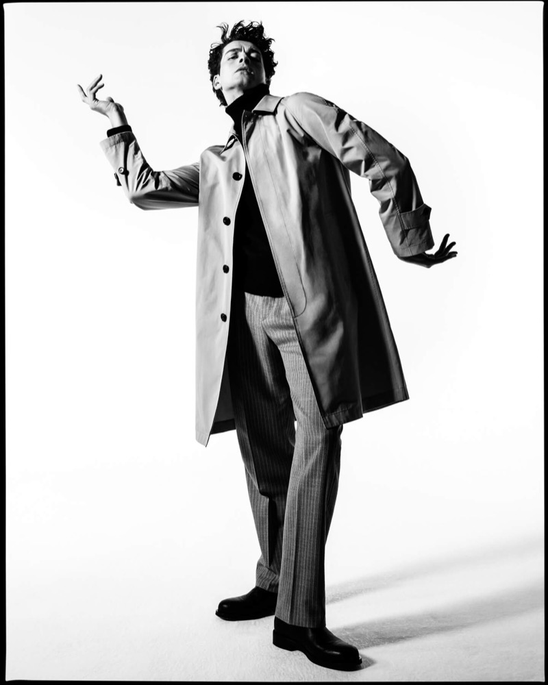 Clarke wears a Burberry Camden car coat over pinstripe trousers with arms spread wide