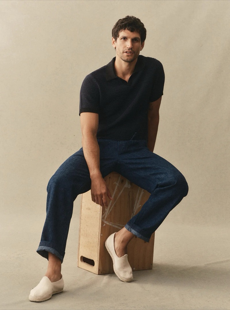 A man wears a dark navy ribbed knit polo with wide-leg dark indigo jeans and white espadrilles for Taylor Stitch summer 2026