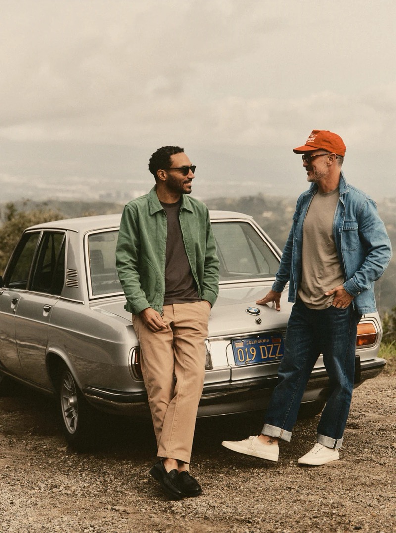 Two men lean against a vintage BMW — one in a green overshirt with khaki trousers, the other in a denim overshirt with jeans — for Taylor Stitch summer 2026