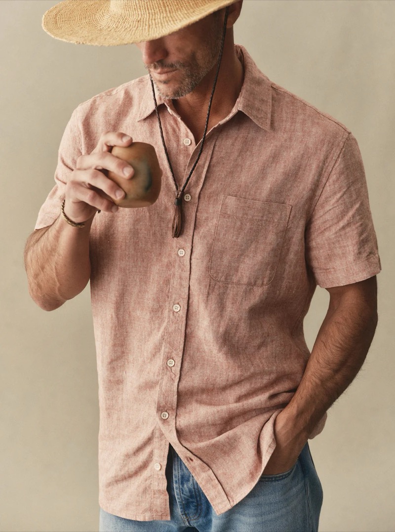 Close-up of a man in a washed pink linen shirt and straw hat holding a drink for Taylor Stitch summer 2026
