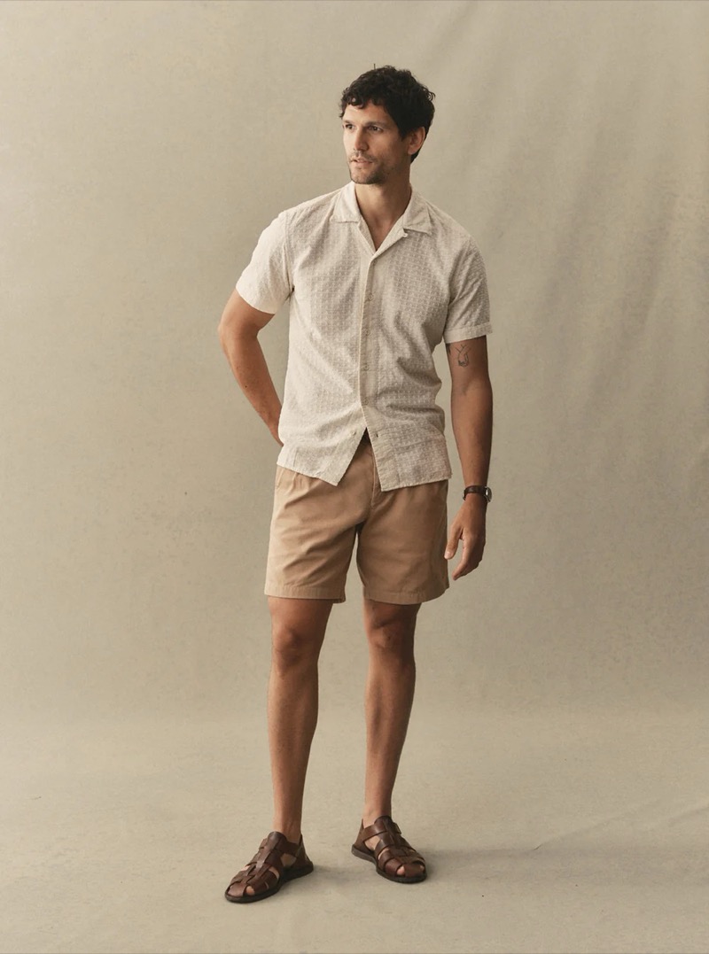 A man in a cream printed camp collar short-sleeve shirt and tan chino shorts with dark brown fisherman sandals for Taylor Stitch summer 2026