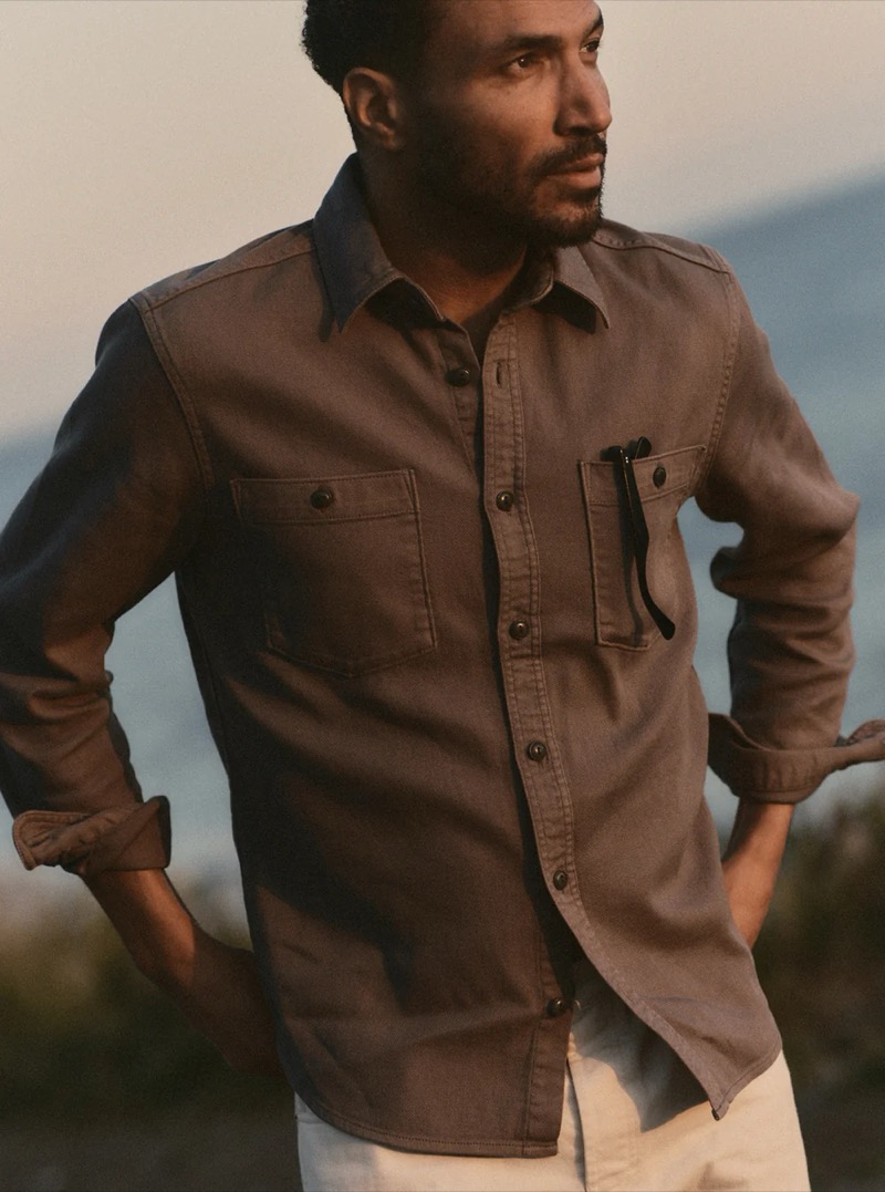 Close-up of a man in a brown utility CPO shirt with snap chest pockets against a golden-hour mountain backdrop for Taylor Stitch summer 2026