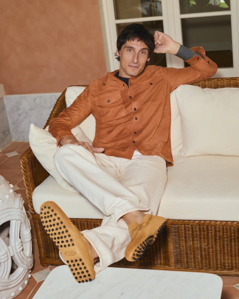 Davide wears a Tod's rust Pashmy leather overshirt with cream trousers and brown Gommino loafers, seated on a wicker sofa