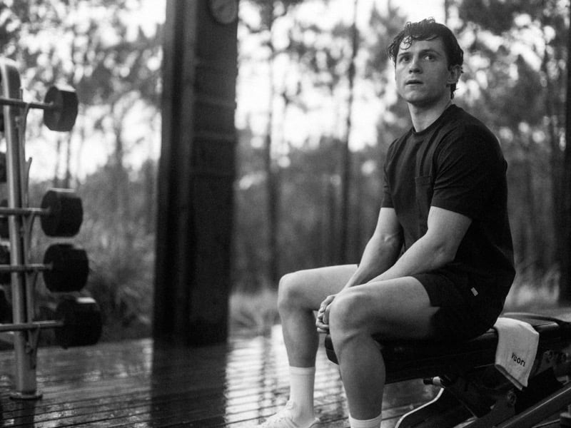 Holland sits on a weight bench in a black pocket tee and black shorts