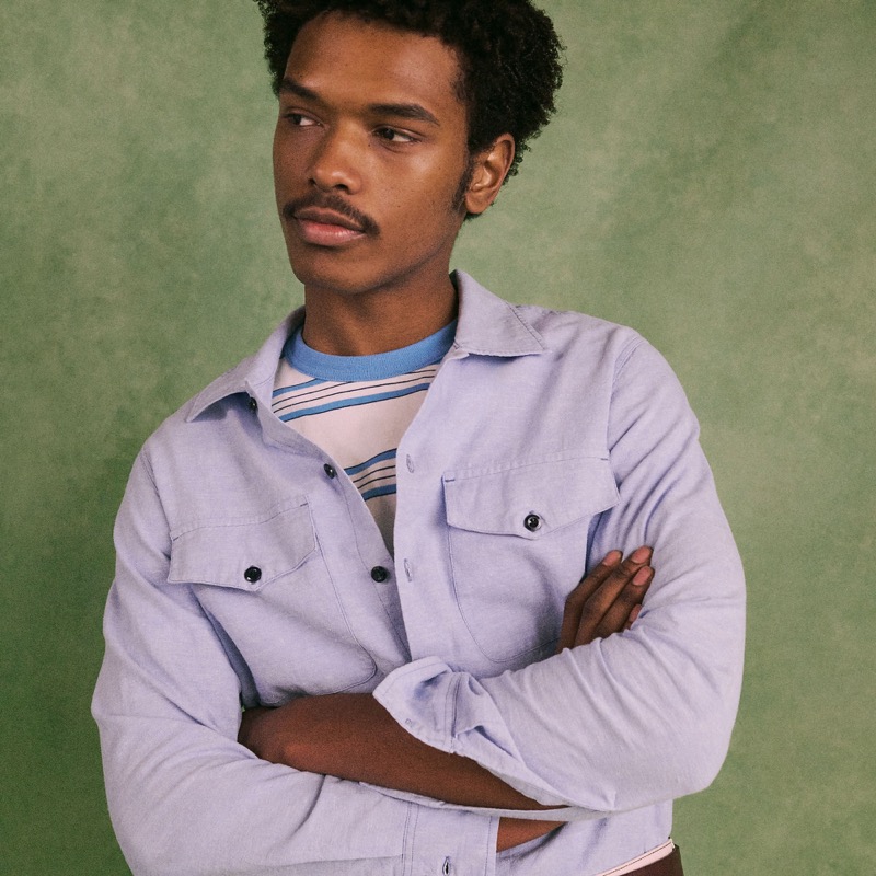 Model wears the Wallace & Barnes Chambray Workshirt in light blue over a striped tee