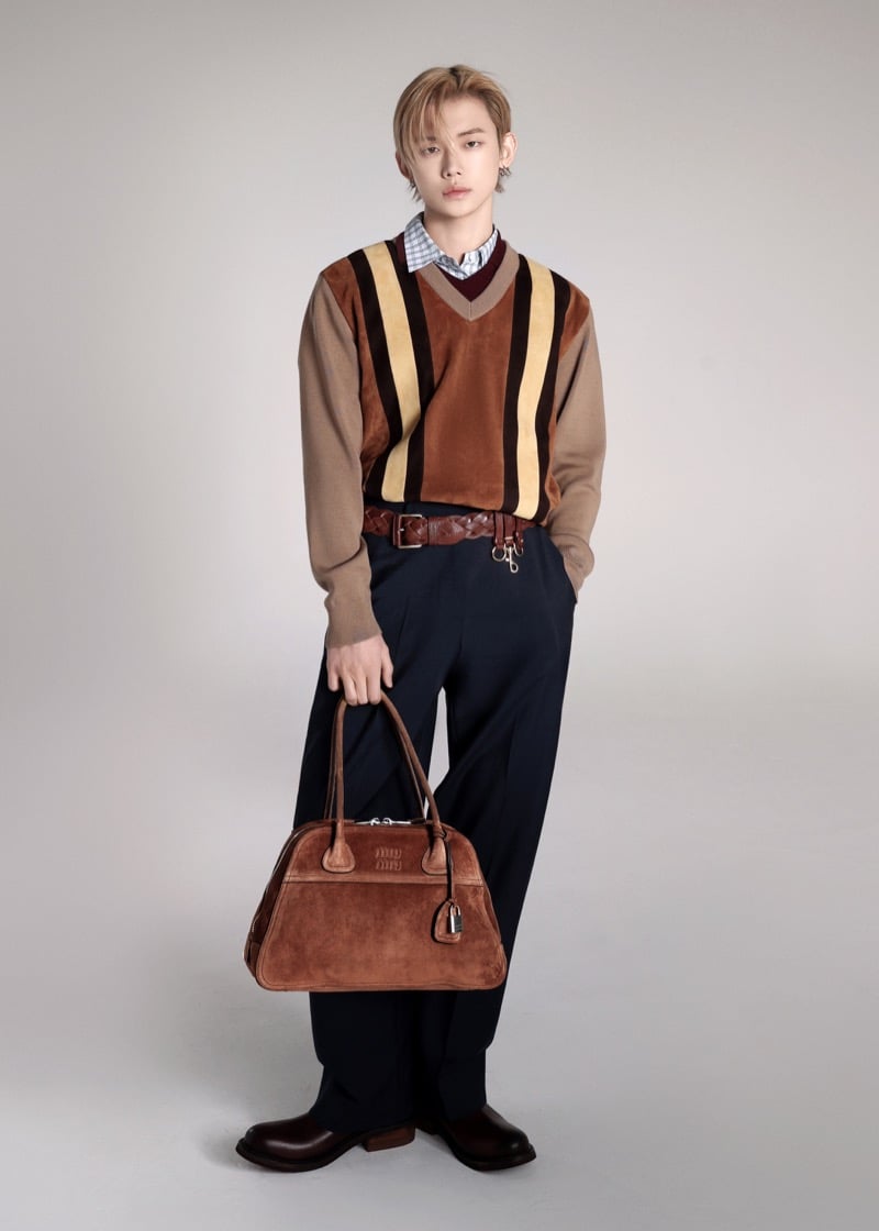 Yeonjun poses full-length in a striped suede Miu Miu V-neck layered over a checked button-down shirt, with a braided leather belt, wide-leg trousers, and a cocoa brown Miu Miu Vivant suede bag