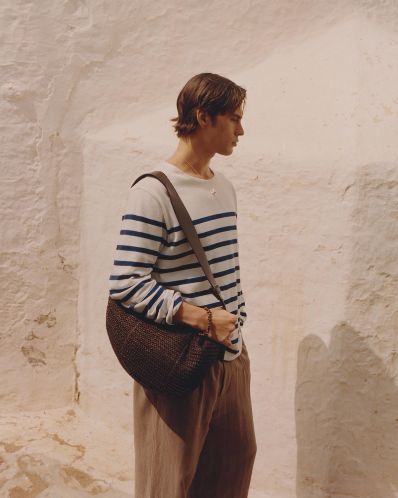 Louis wears a Breton-stripe knit with a dark woven shoulder bag and linen trousers