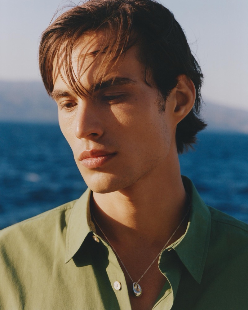 Louis wears an olive linen shirt with a stone pendant necklace in a close-up portrait