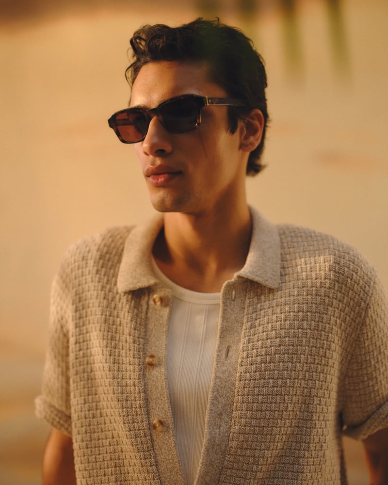 Mase wears tortoise Abercrombie & Fitch square sunglasses with an oatmeal waffle-knit button-through sweater polo open over a white ribbed tank, lit by warm sunset light