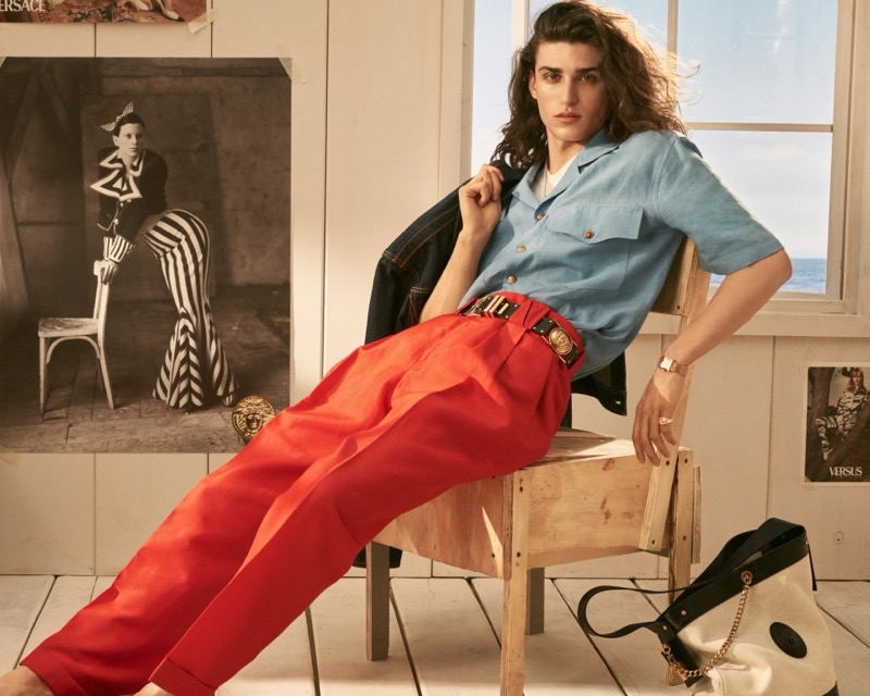 Alvise wears a blue linen camp collar shirt with red pleated trousers from the Versace La Vacanza collection for 2026
