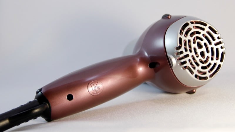 close-up of a rose-pink blow dryer lying on its side against a pale background, showing the circular rear air-intake filter at the base of the barrel