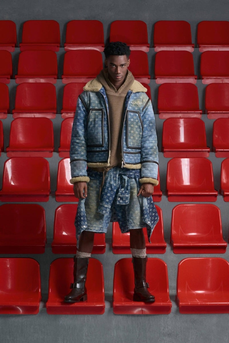 Nehemiah Kargbo wears a Dsquared2 monogram denim jacket with shearling-trimmed collar over a tan hooded sweatshirt with matching monogram denim shorts and brown leather buckle boots