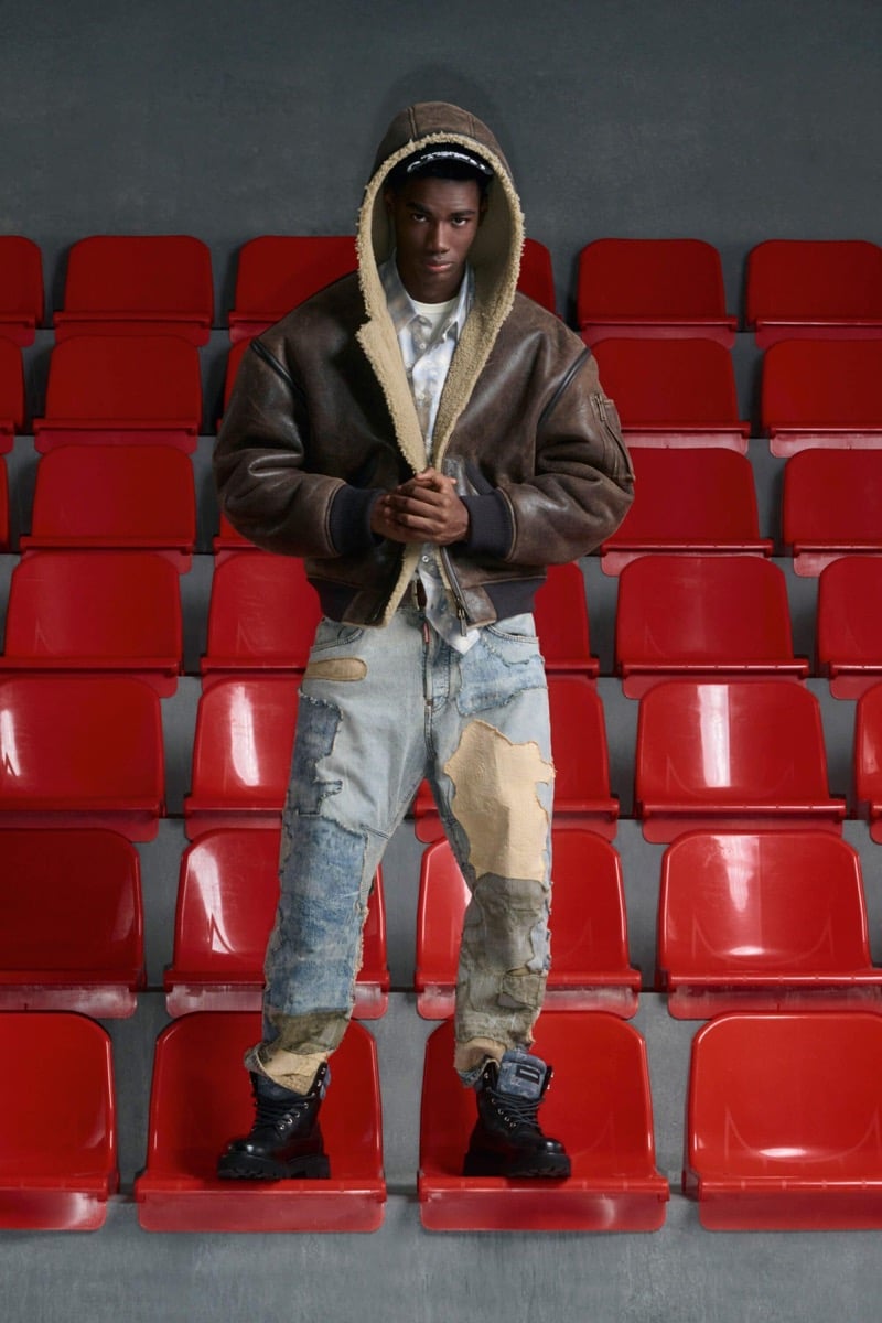 Nehemiah Kargbo wears a brown leather hooded bomber with cream shearling lining over a white shirt with patchwork distressed jeans and black hiking boots
