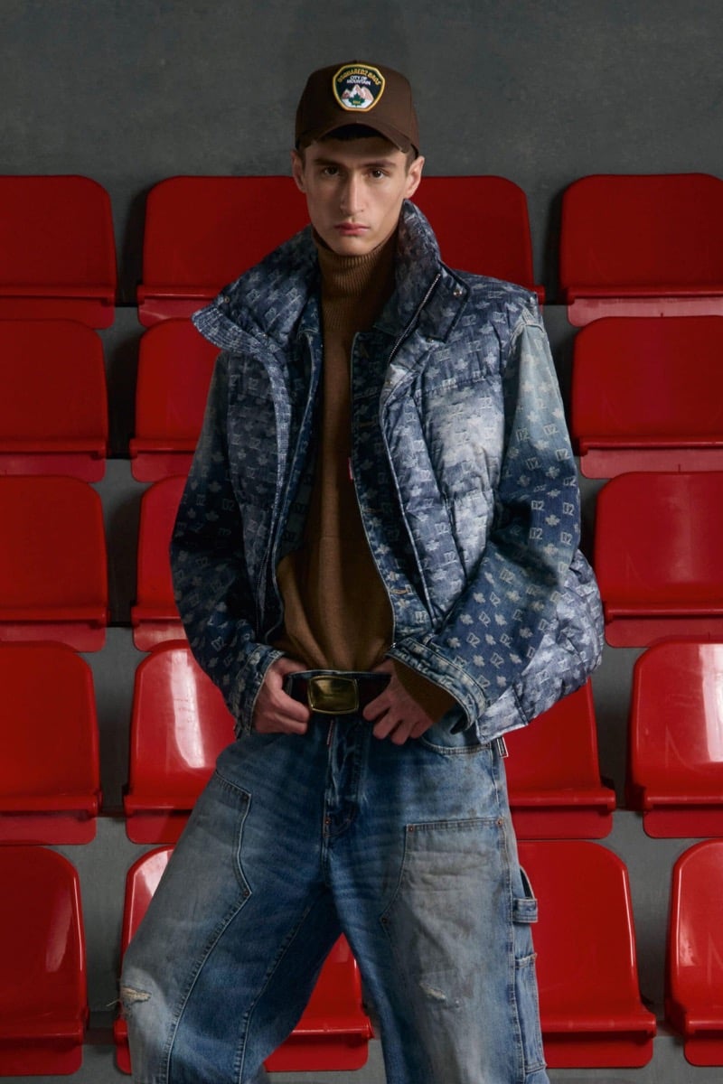 Madson Santos wears a brown patch baseball cap and Dsquared2 monogram denim puffer and brown turtleneck with baggy carpenter jeans