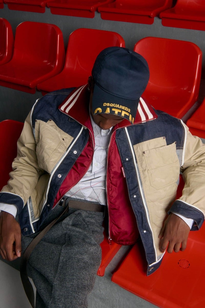 Nehemiah Kargbo wears a navy baseball cap and patchwork denim and tan canvas colorblock jacket with red lining over a white shirt with gray wool trousers