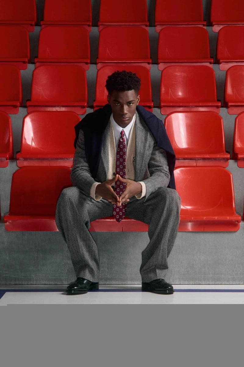 Nehemiah Kargbo wears a gray herringbone three-piece suit, a white shirt, and a burgundy diamond-print tie with black dress shoes