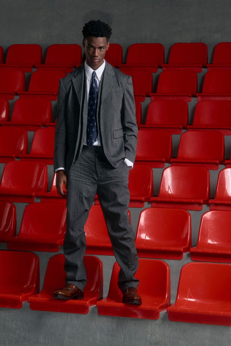 Nehemiah Kargbo wears a charcoal gray three-piece suit over a white shirt with a navy printed tie and brown leather dress shoes