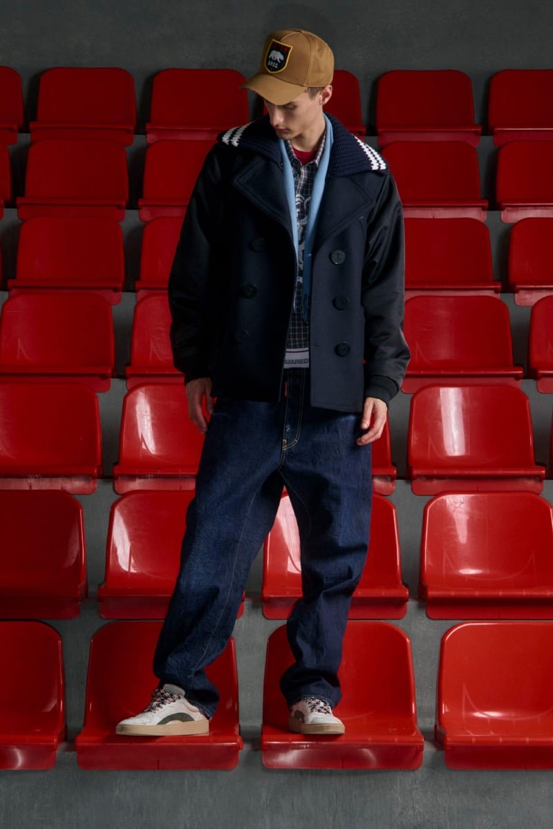 Madson Santos wears a tan suede patch cap and navy peacoat with cream and navy striped knit collar over a plaid shirt with denim jeans and white sneakers