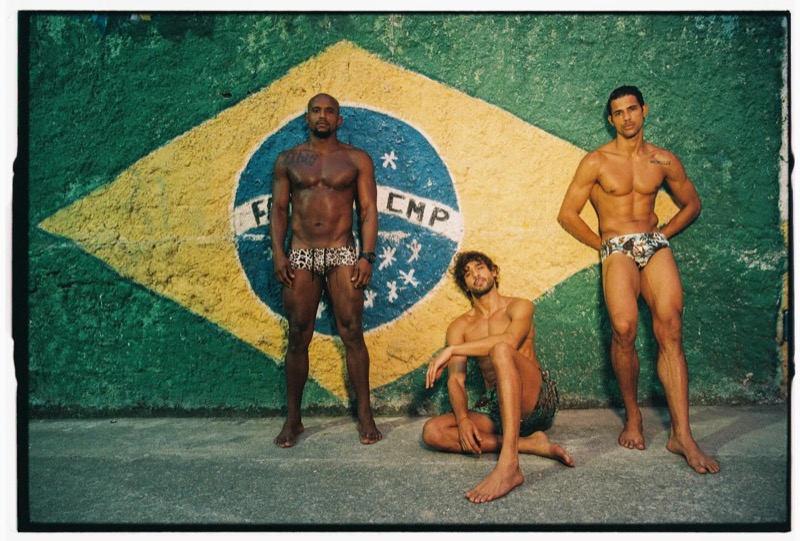 Geremias, Marlon, and Jonas pose in front of a hand-painted Brazilian flag mural in Dsquared2 summer 2026 beachwear — leopard-print briefs, low-slung printed trunks, and tropical-print briefs