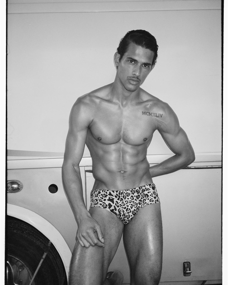 Jonas leans against a vintage white car in leopard-print Dsquared2 swim briefs, his MCMXLIV chest tattoo visible in the black-and-white frame