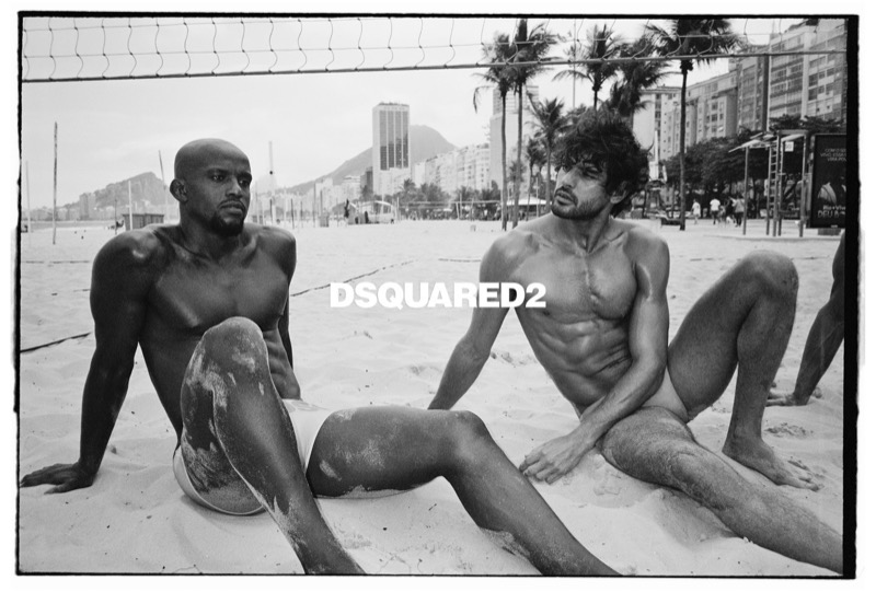 Geremias and Marlon sit on the sand of a Rio beach beneath a volleyball net, palm trees and Copacabana high-rises behind them, the Dsquared2 logo set between their shoulders