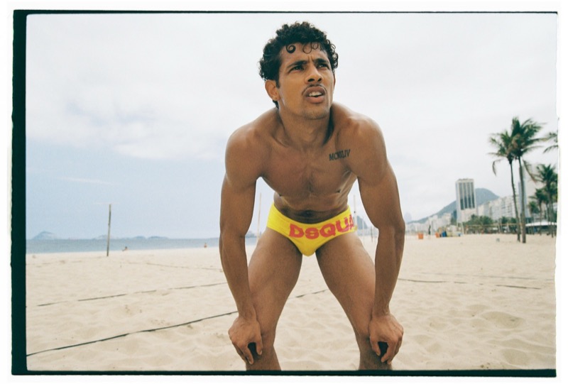 Jonas in yellow Dsquared2 logo swim briefs crouches forward on a Rio beach volleyball court