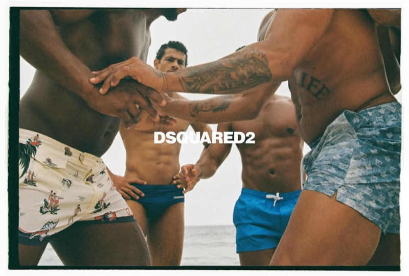 Cropped torso shot of four shirtless men clasping hands in a circle on a Rio beach in Dsquared2 swimwear