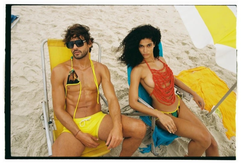 Marlon reclines in a yellow beach chair in bright yellow Dsquared2 swim shorts and black sunglasses beside Raynara, who wears a red crocheted bralette