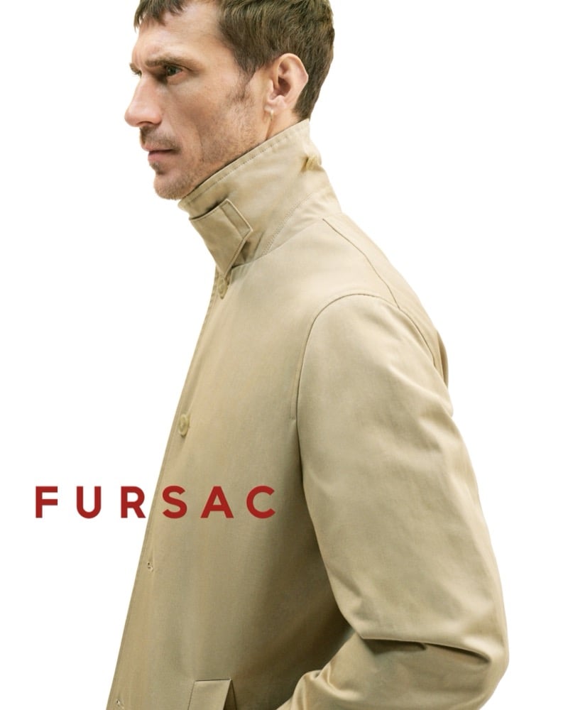 Severe side profile of Clément in a tan cotton stand-collar mac with the collar fastened high against the neck