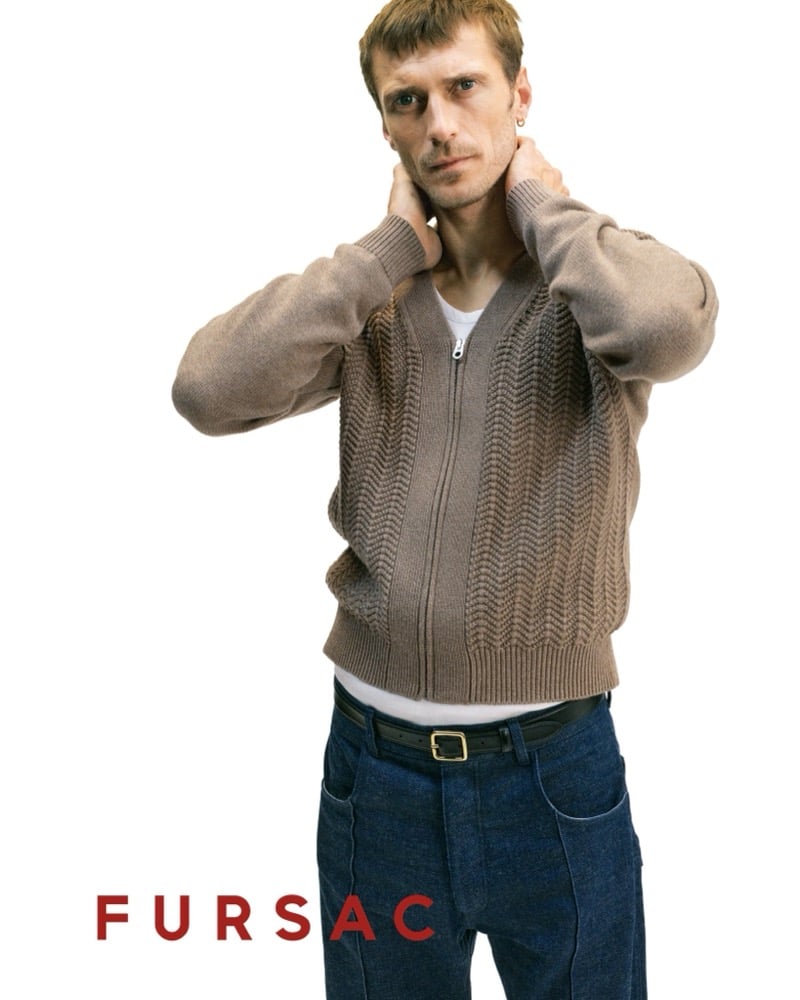 Clément wears a taupe waffle-knit zip cardigan over a white tee with indigo jeans and a black leather belt with gold buckle