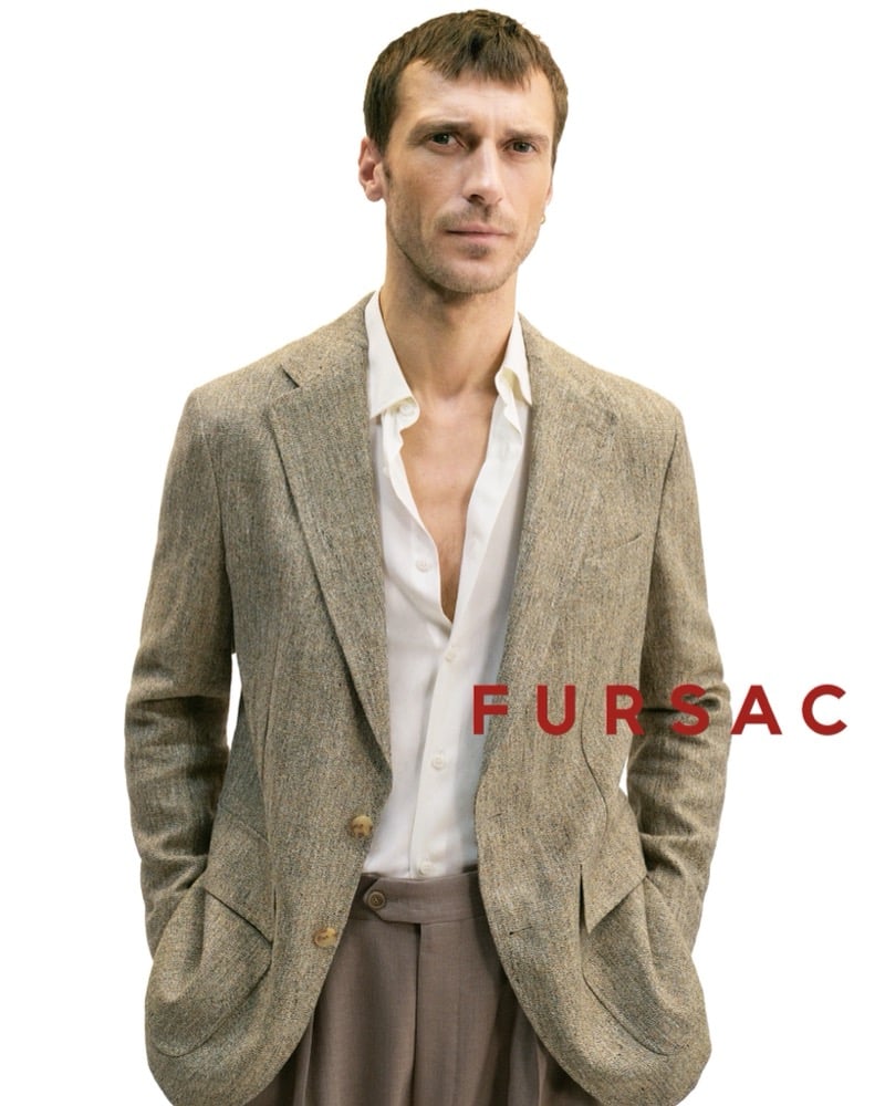 Clément wears a flecked tweed blazer over an open white shirt and taupe pleated trousers cut wider through the leg