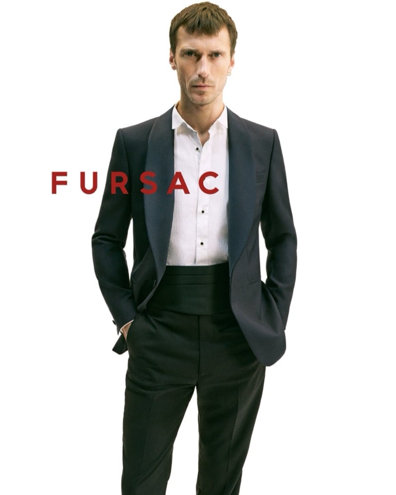 Clément wears a peak-lapel tuxedo jacket with a white pleated tuxedo shirt, black studs, a black cummerbund, and black trousers