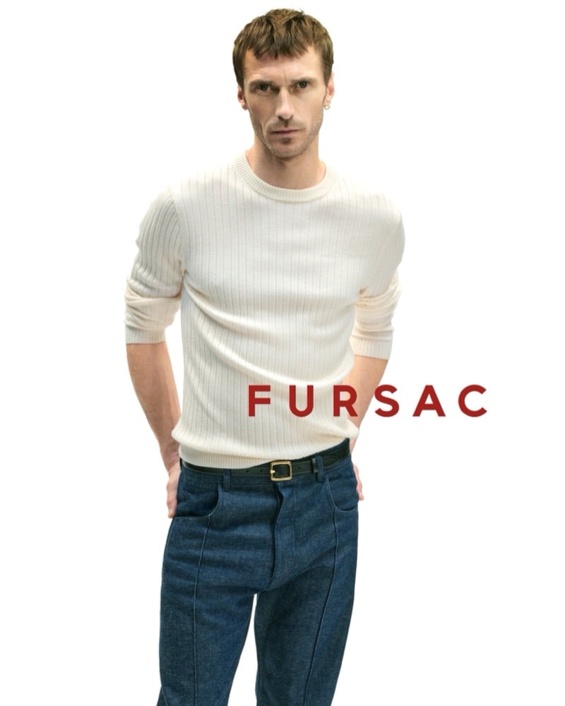 Clément wears a cream ribbed wool crewneck sweater with indigo jeans and a black leather belt with gold buckle