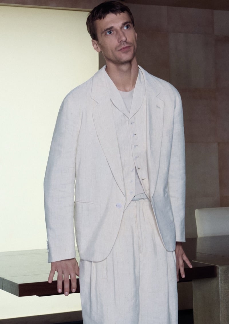 Clément stands at a wooden desk in a Giorgio Armani cream linen three-piece suit with a soft tee underneath