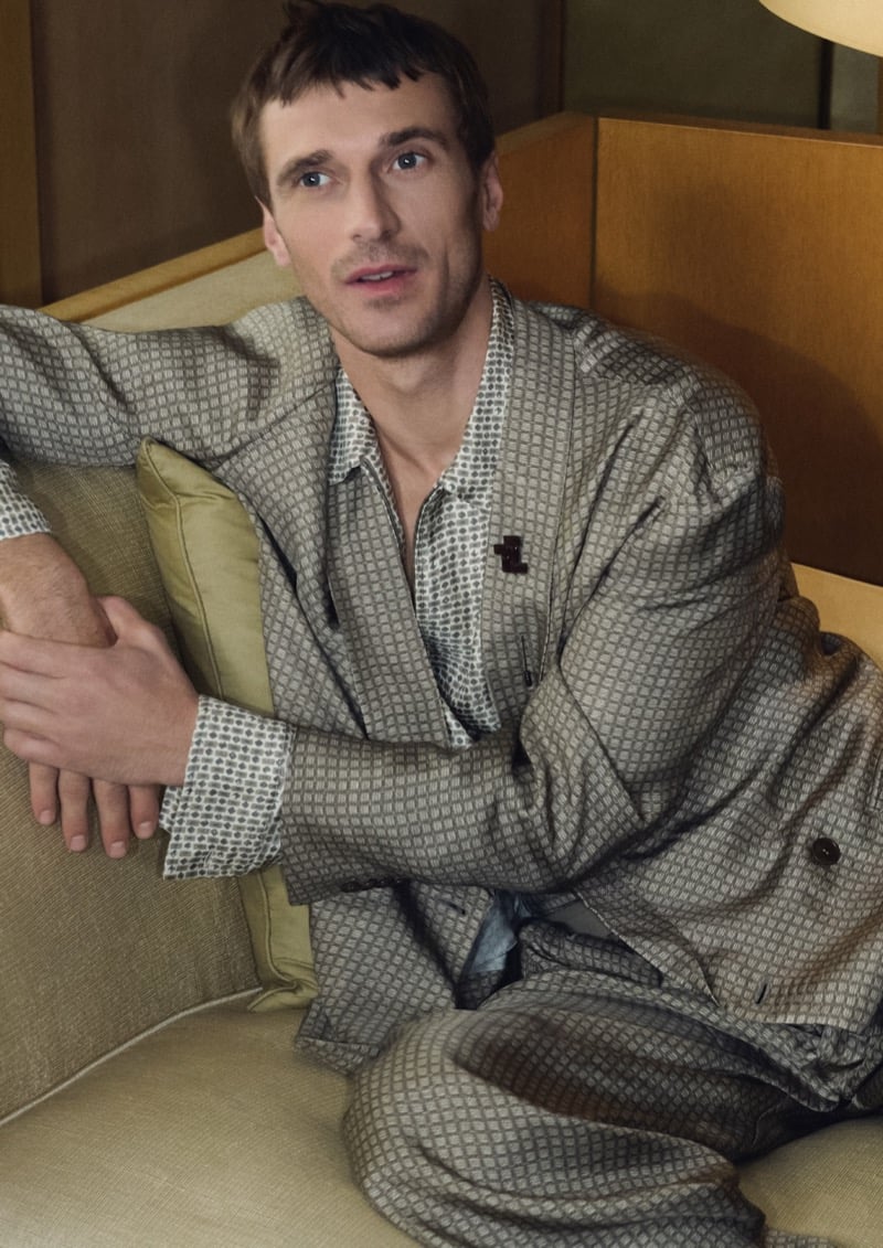 Clément reclines on a sage sofa in a Giorgio Armani geometric-printed silk shirt and matching trousers under a warm lamp