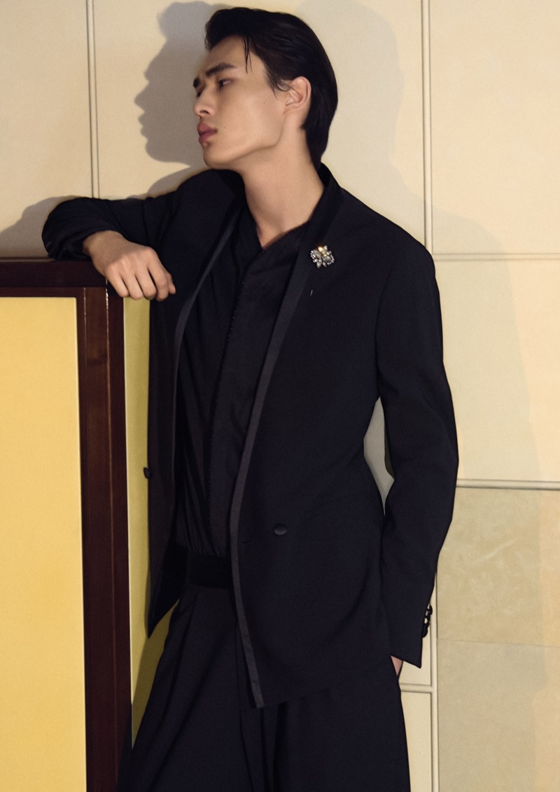 Zhaoyi leans against a yellow door in a black Giorgio Armani jacket with a satin sash and jeweled brooch at the collar