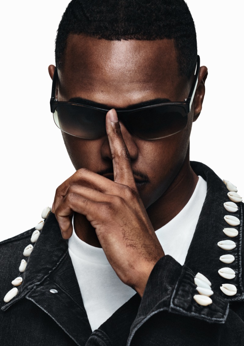 Close portrait of TZ in black sport sunglasses and a black denim jacket trimmed with rows of white cowrie shells over a white tee