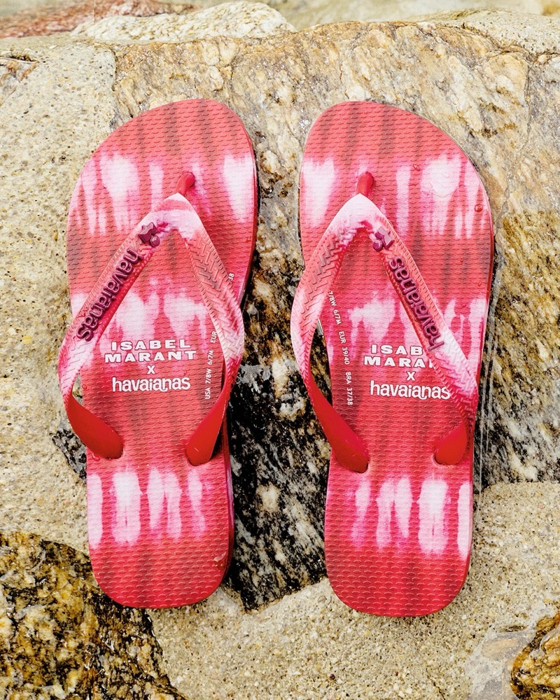 Close-up of the red and white tie-dye Isabel Marant x Havaianas thong sandals set on weathered gray and tan beach rocks