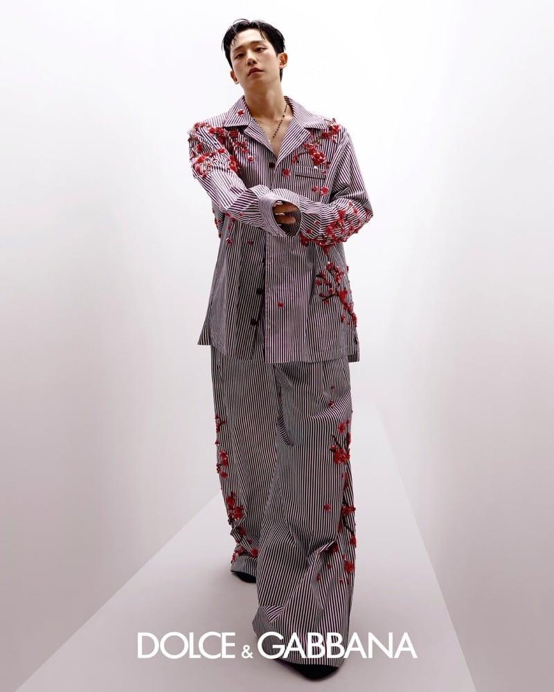 Jung stands with arms crossed in a black and white pinstripe oversized camp-collar shirt scattered with red three-dimensional flower embellishments, paired with matching striped wide-leg trousers and a delicate gold pendant chain