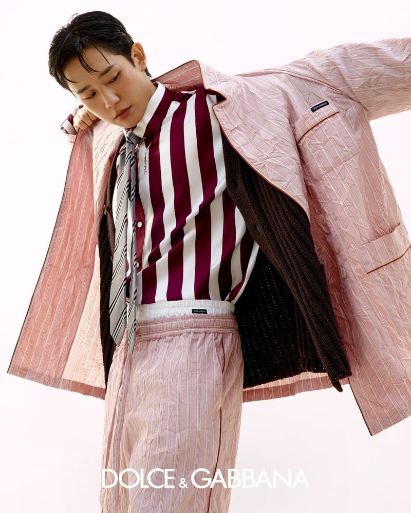 Jung tilts his head to one side in the same pink pinstripe quilted suit pulled across one shoulder, revealing a wide burgundy and white striped satin shirt, a gray diagonal stripe tie, and a brown ribbed cardigan layered underneath