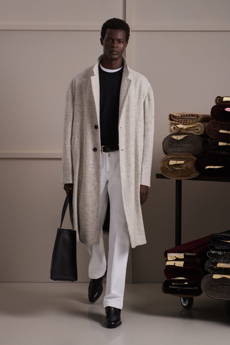 Mohammed Abubakar wears a cream donegal tweed overcoat over a black crewneck and white tee with white trousers and black loafers
