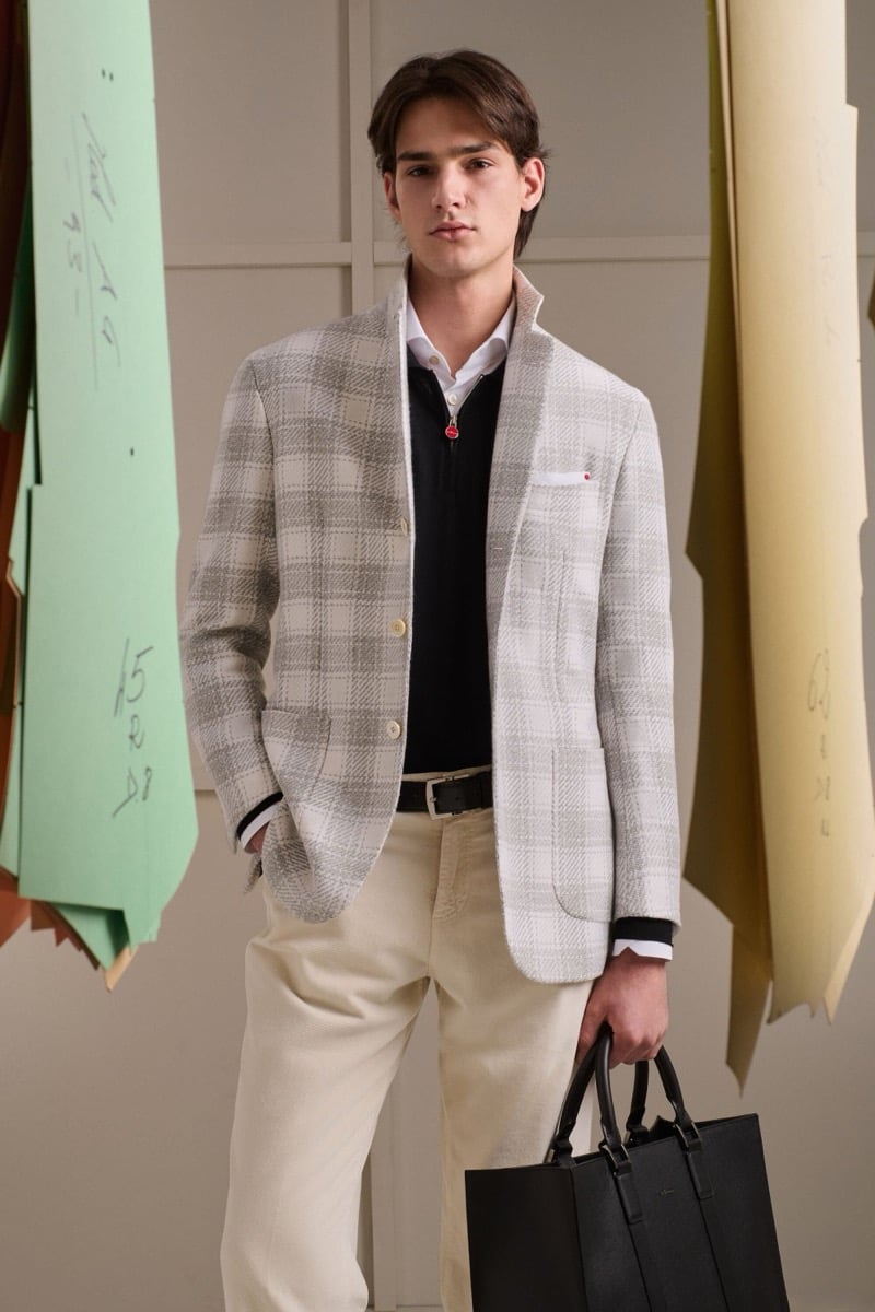 Noah Herbst wears an oatmeal Prince of Wales check jacket over a white shirt and navy half-zip sweater with beige corduroy trousers
