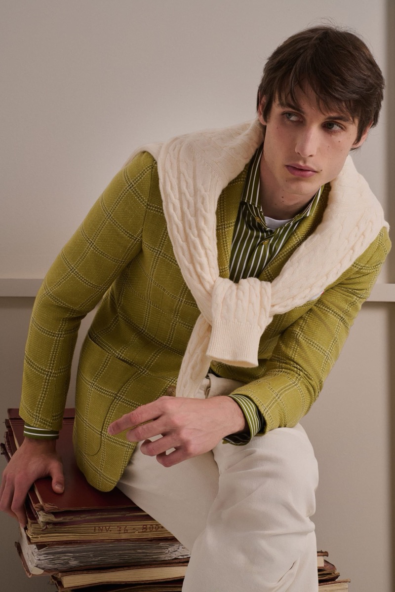 Unai Bartra wears a chartreuse windowpane knit jacket over a green striped shirt with a cream cable-knit sweater knotted over the shoulders and ivory corduroy trousers