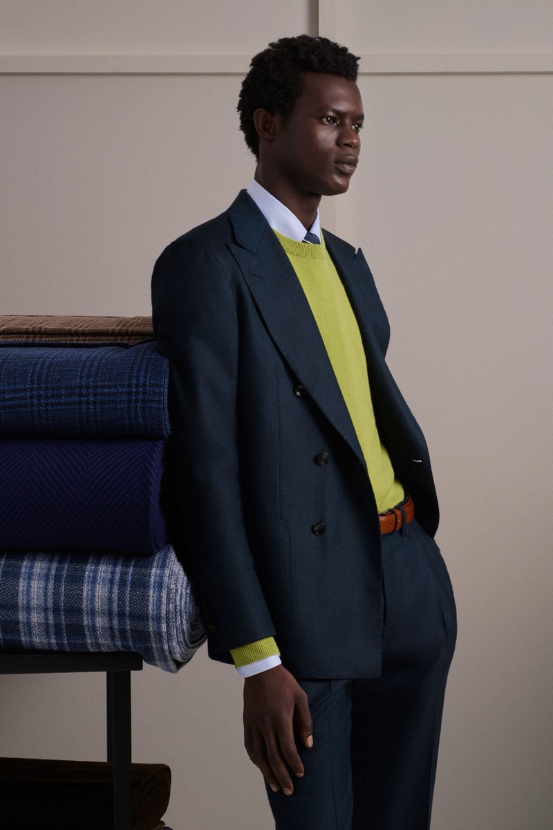 Mohammed Abubakar wears a navy double-breasted suit over a chartreuse crewneck sweater and white shirt with a tan leather belt