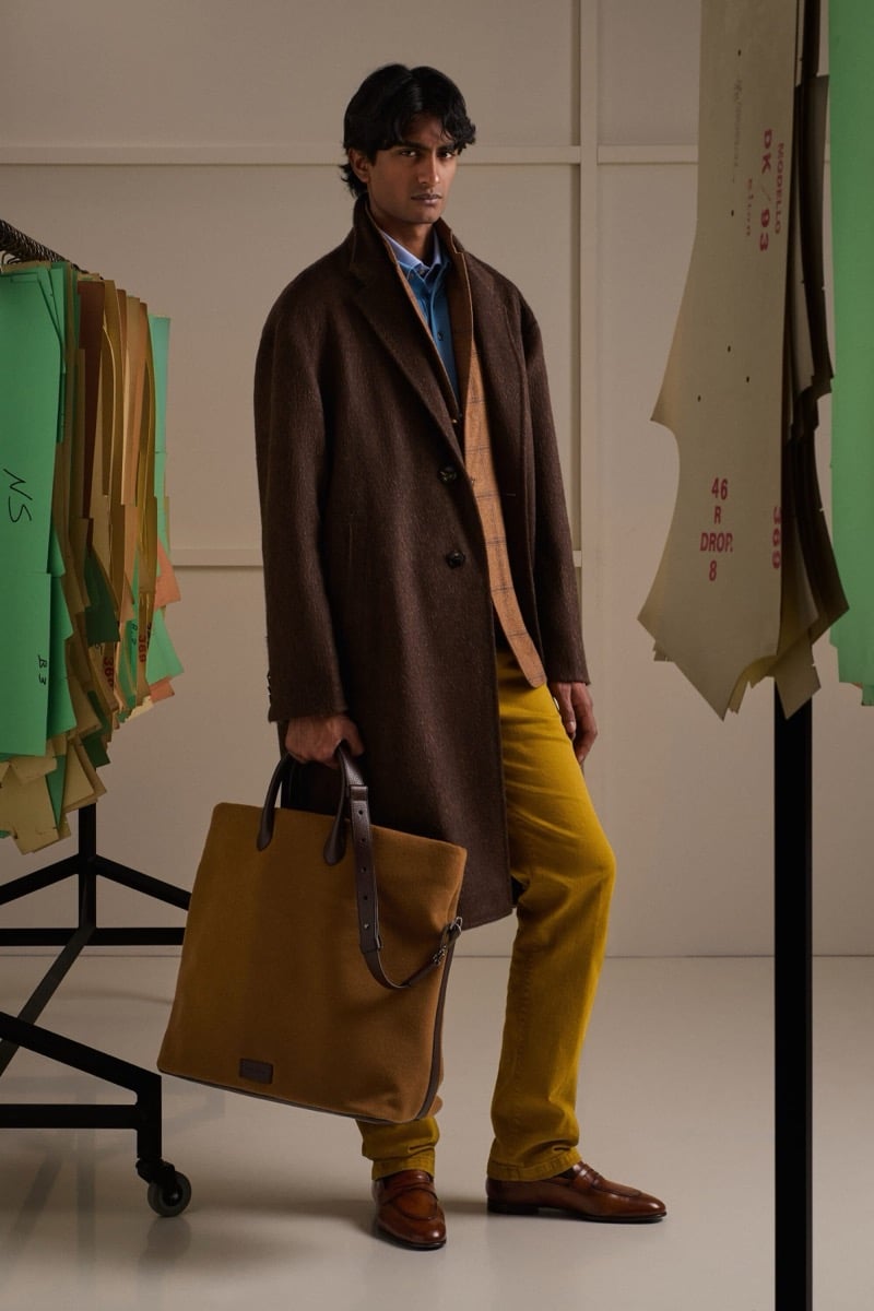 Rishi Robin wears a brown wool single-breasted overcoat over a beige plaid blazer with a blue shirt and mustard yellow corduroy trousers