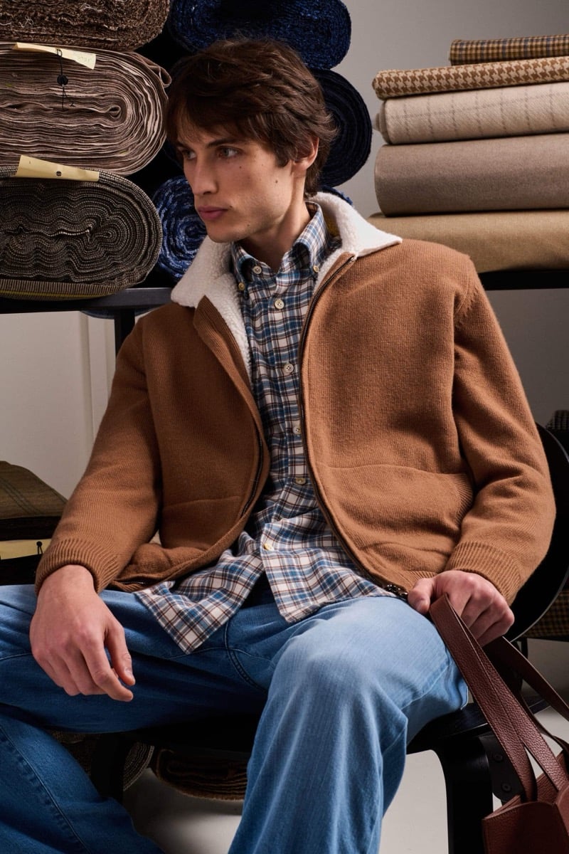 Unai Bartra wears a tobacco knit blouson with a cream sherpa shawl collar over a blue plaid flannel shirt and washed denim jeans