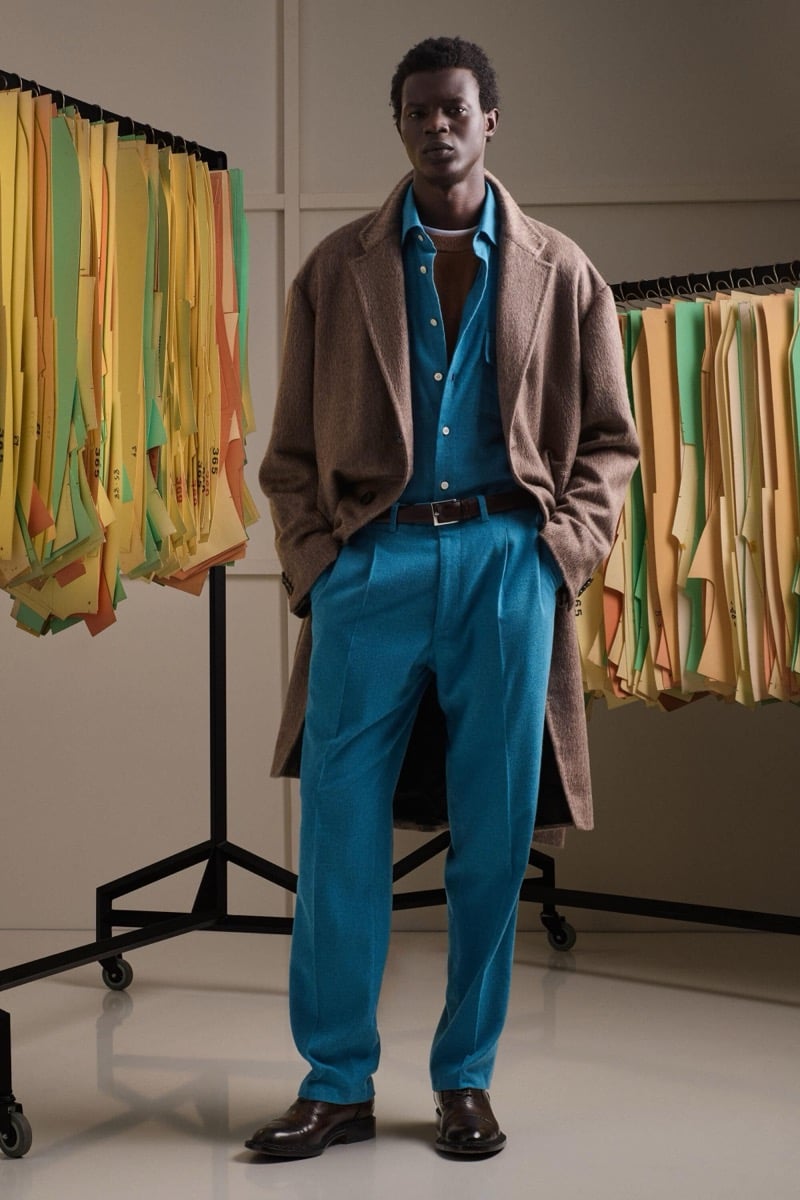 Mohammed Abubakar wears a taupe alpaca single-breasted overcoat over a teal shirt and matching teal pleated trousers with brown loafers
